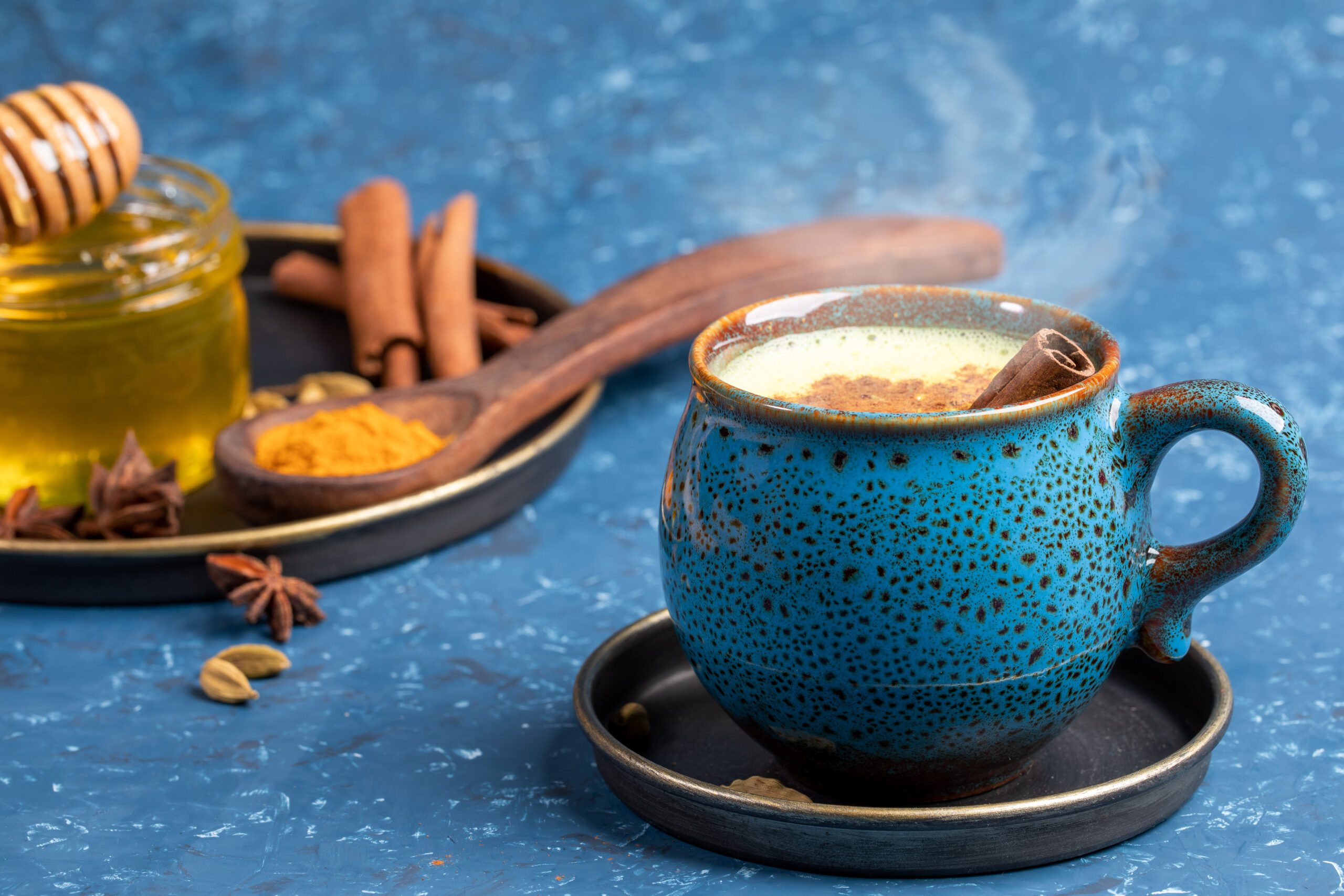 Cup of traditional Indian hot drink golden turmeric milk with cinnamon, turmeric, anise and honey on blue background. Golden Milk
